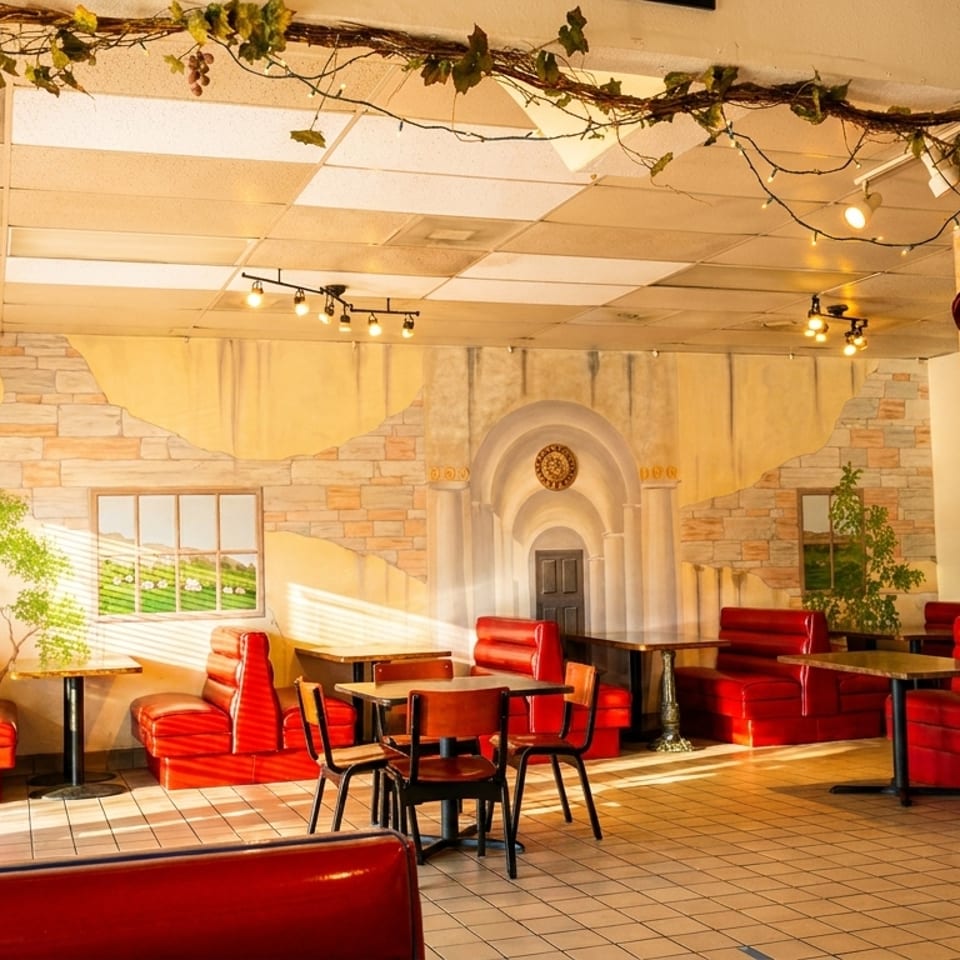 Bright restaurant dining room with red booths, tiled floors, muralled walls, vine decorations, and a gumball machine.