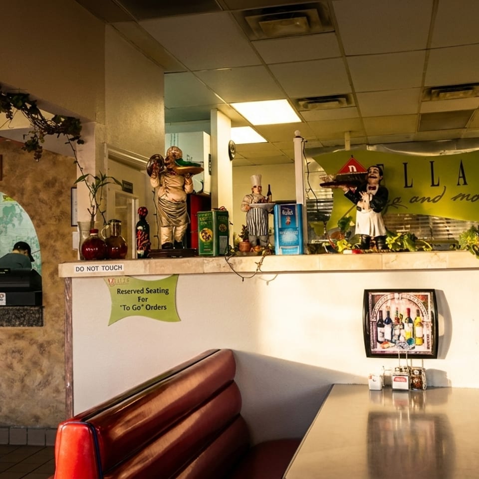 Retro pizzeria dining area with red booths, a set table, decorative chef figurines, and a colorful pizza-themed sign.