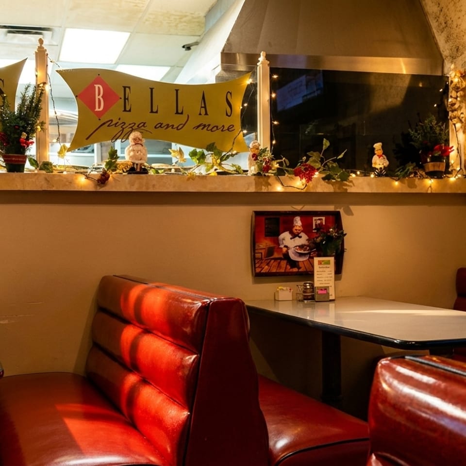 Cozy Bella’s pizza restaurant dining area with red leather booths, tables, festive decorations, and branded wall signs.